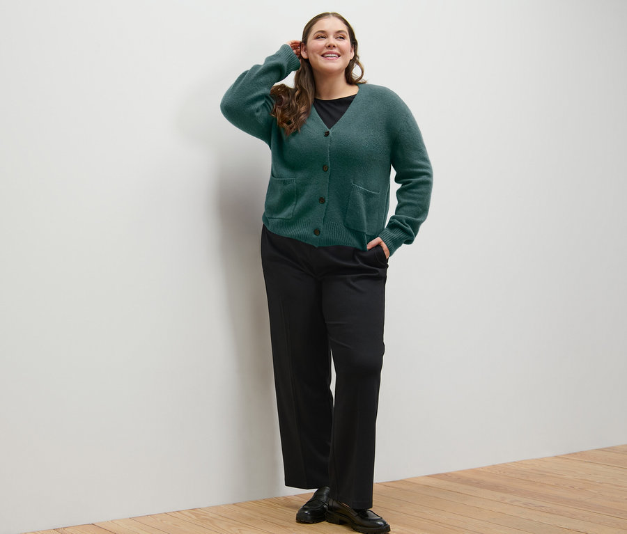 Žena pózuje v tmavozelenom pletenom svetri s vlnou a pohodlných džersejových nohaviciach.
