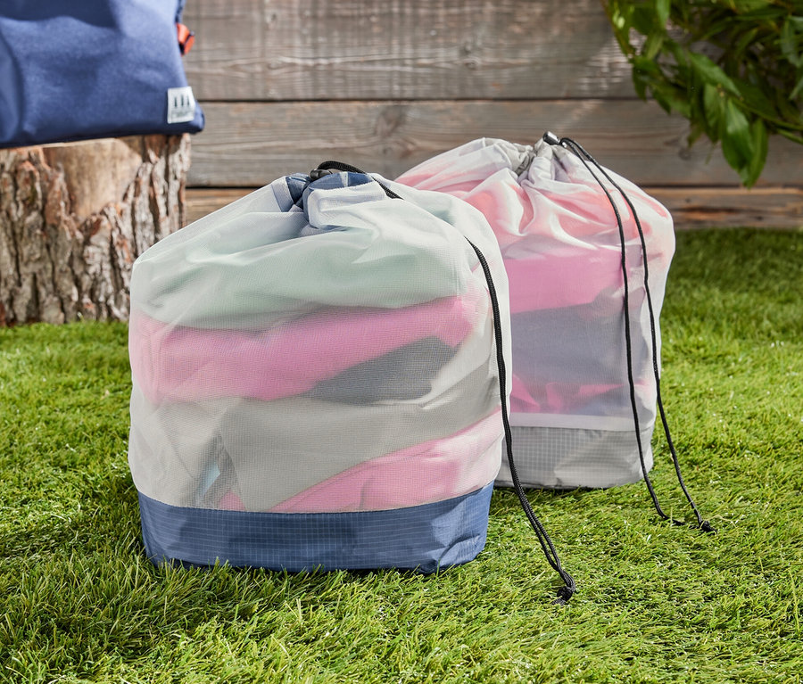 Dve outdoorové vrecká zo sieťoviny na tráve, v pozadí batoh.