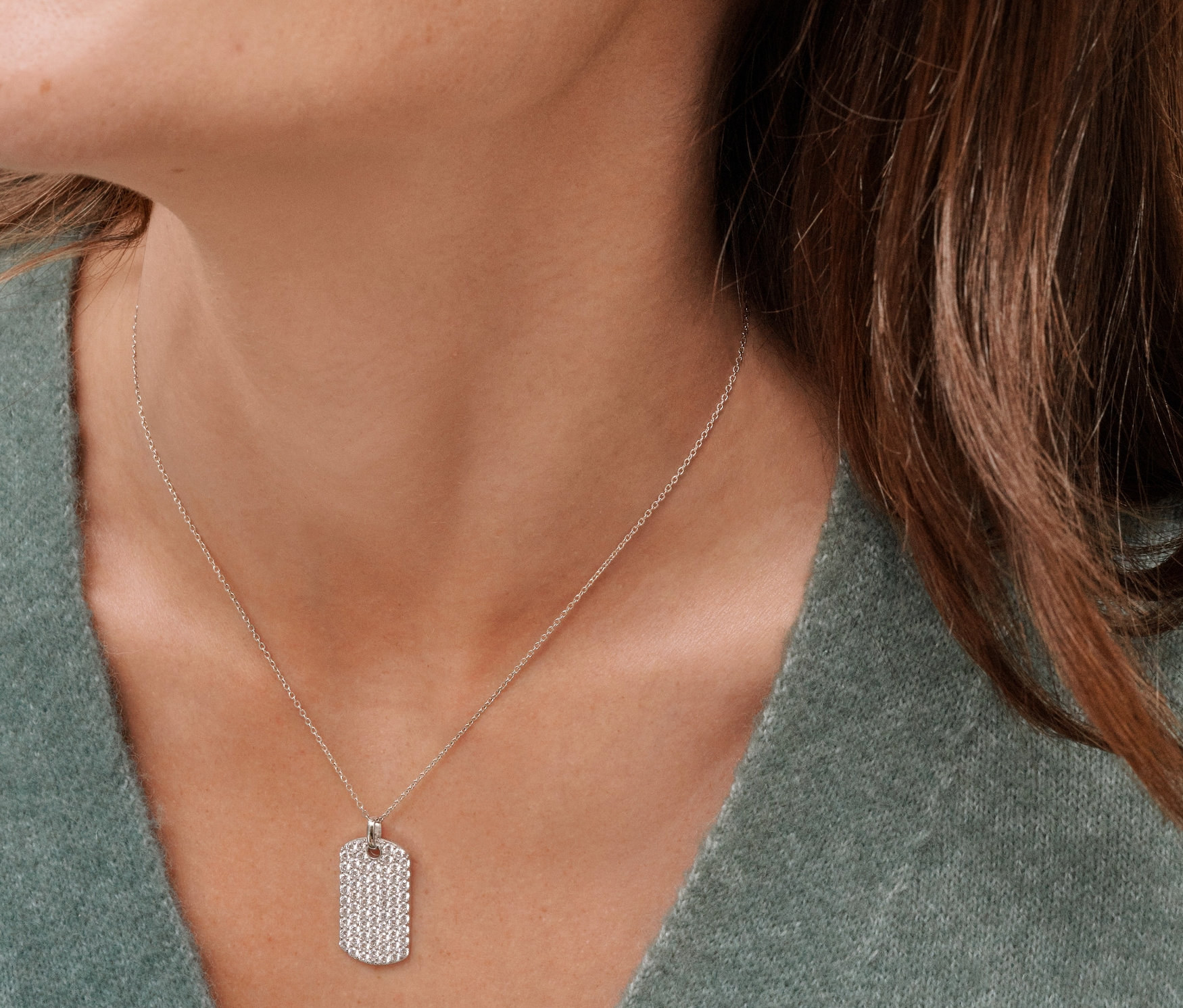 Usmievajúca sa žena má na sebe ródiované strieborné kónické náušnice kreoly so zirkónmi a dva ródiované strieborné náhrdelníky so zirkónmi.