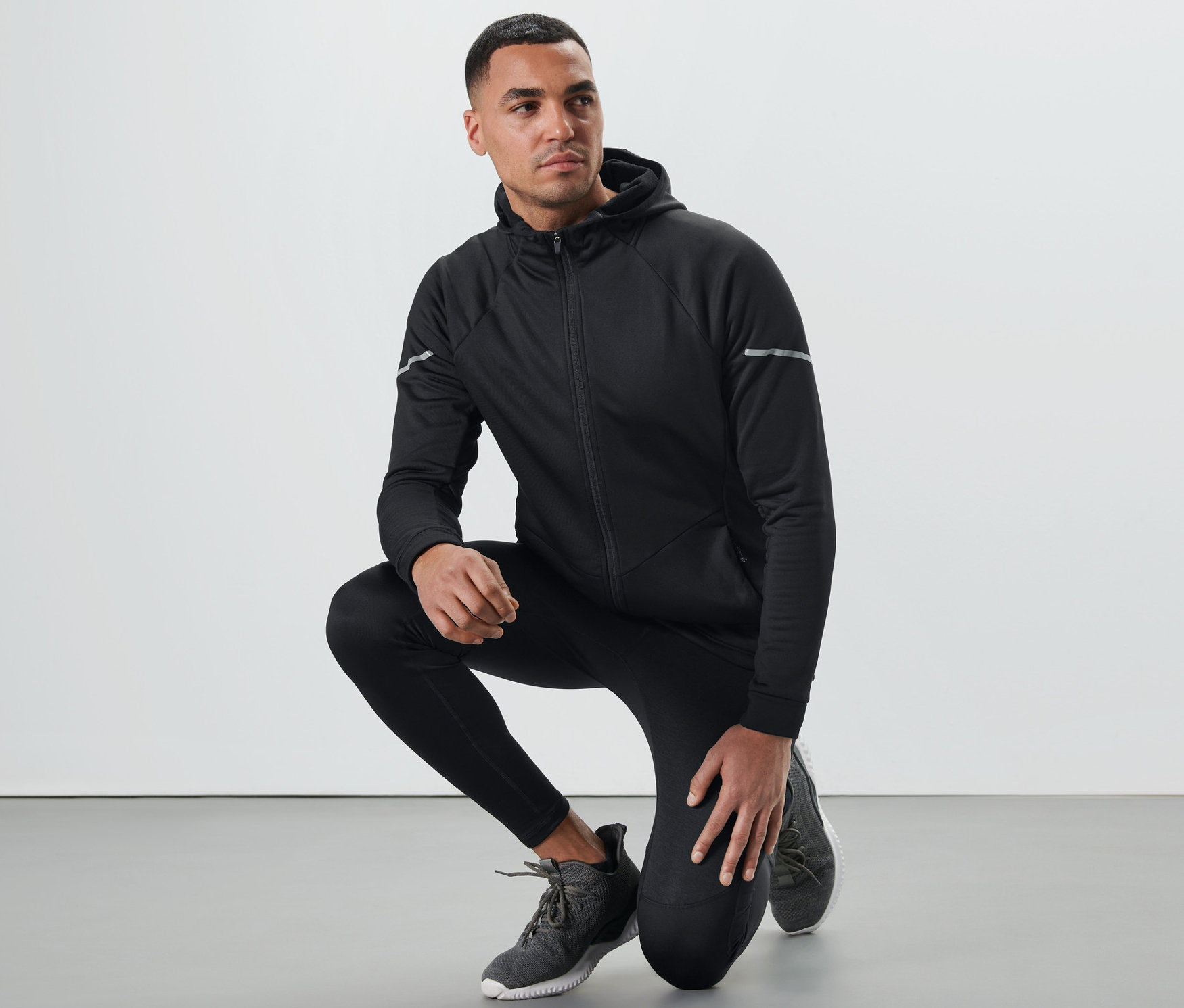 Muž v čiernej termobunde kľačí.