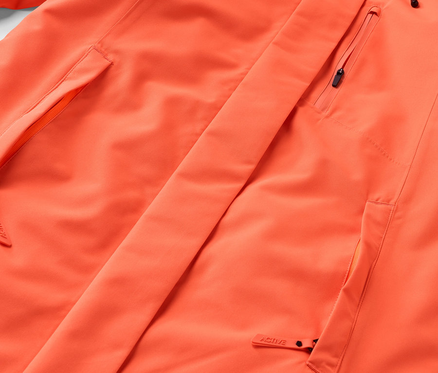 Detail oranžovej bundy s vreckami a zipsom.