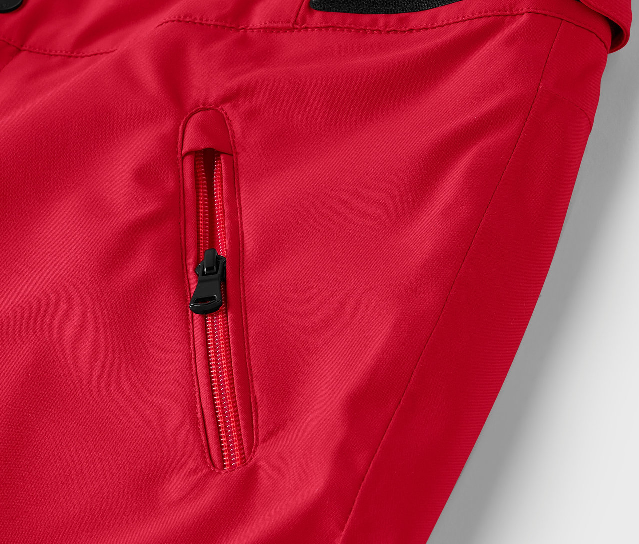 Detail červenej bundy s čiernym zipsom na vrecku.