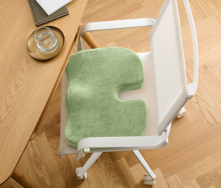 Zelený sedák na stoličke s výrezom v tvare písmena U. Stolička stojí pri drevenom stole.