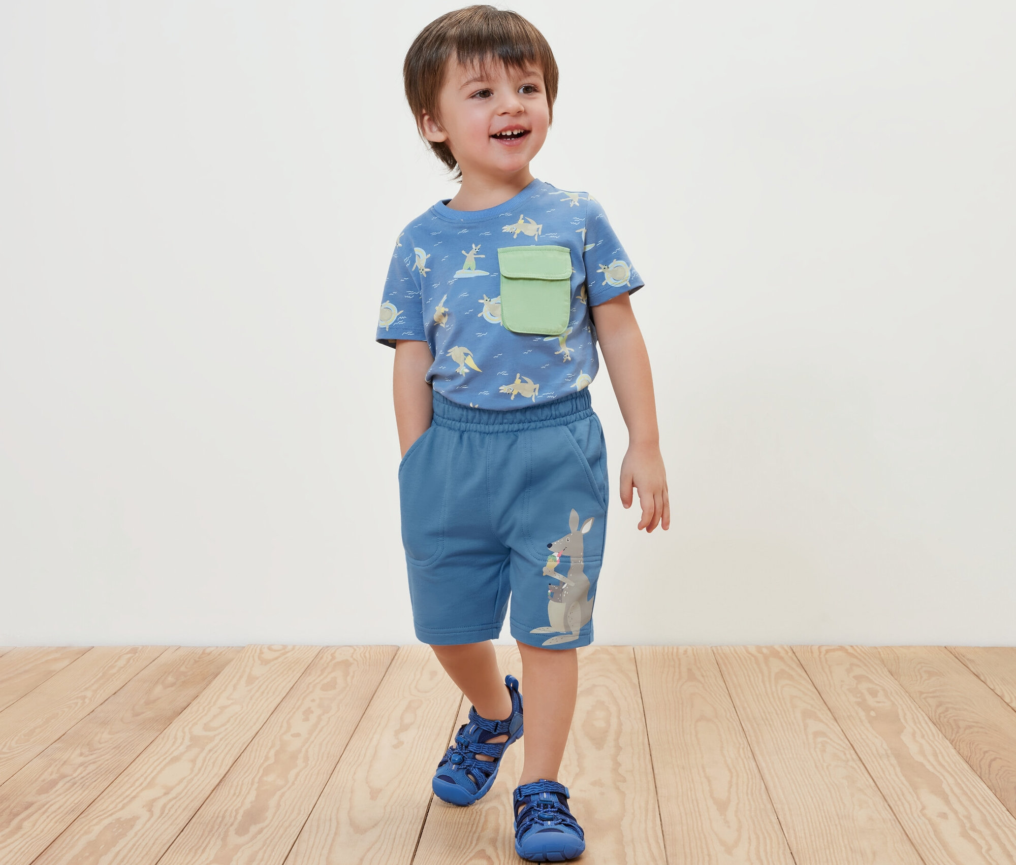 Chlapec stojí a má na sebe modré teplákové šortky a tričko.