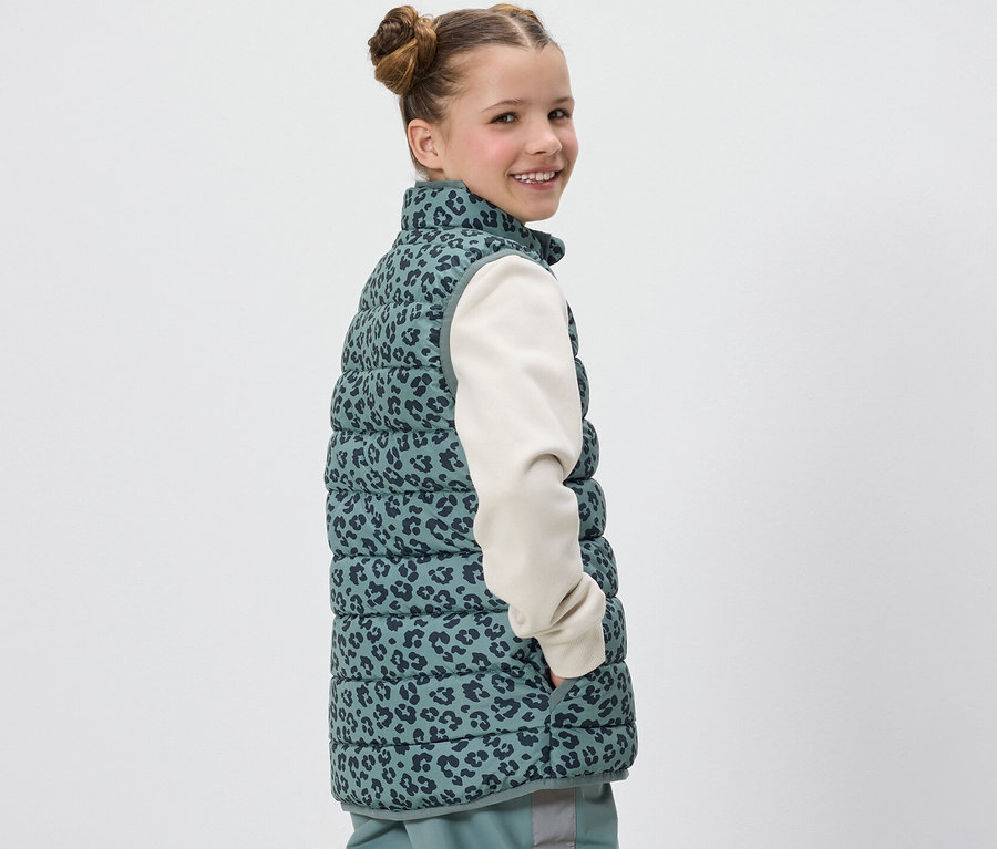 Dievča sa usmieva cez plece a má na sebe prešívanú vestu Kinder s leopardou potlačou.