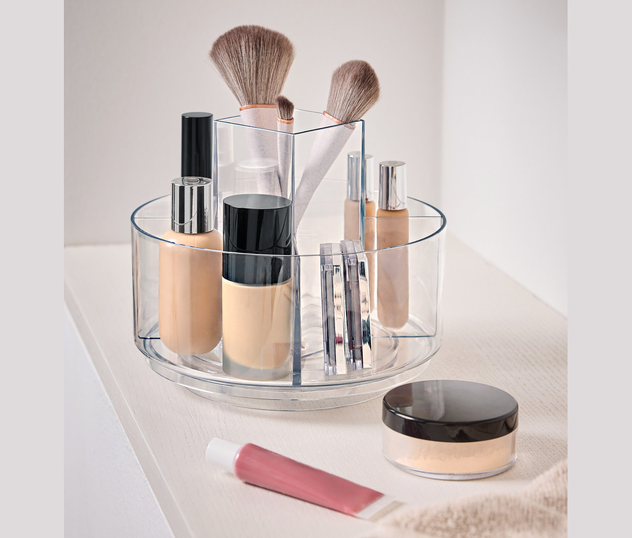 Priehľadná otočná nádoba s kozmetikou na bielom povrchu.