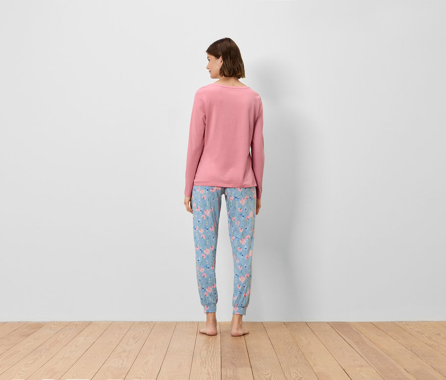 Žena chrbtom k fotoaparátu má na sebe ružový top s dlhým rukávom a modré nohavice s kvetinovým vzorom.