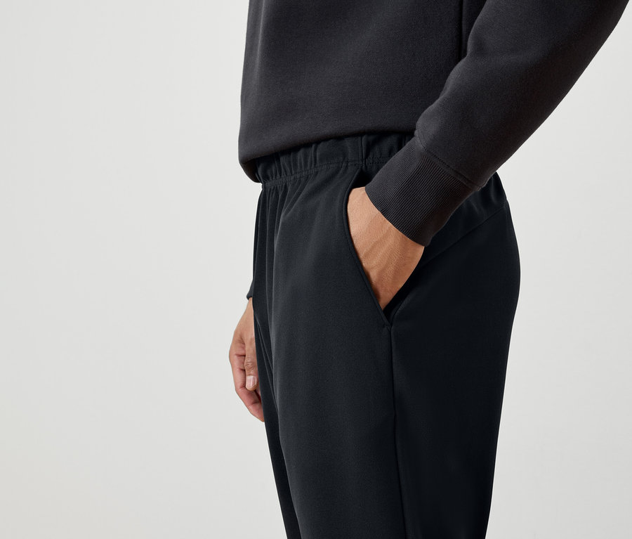 Muž má ruku vo vrecku čiernych teplákov.