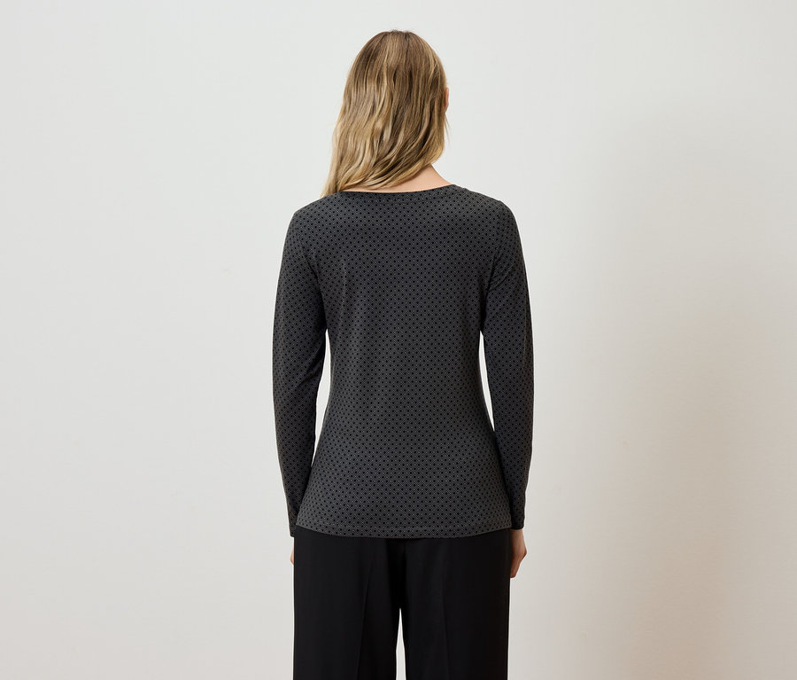 Žena chrbtom k fotoaparátu má na sebe sivo-čiernu blúzku s dlhým rukávom a čierne nohavice.