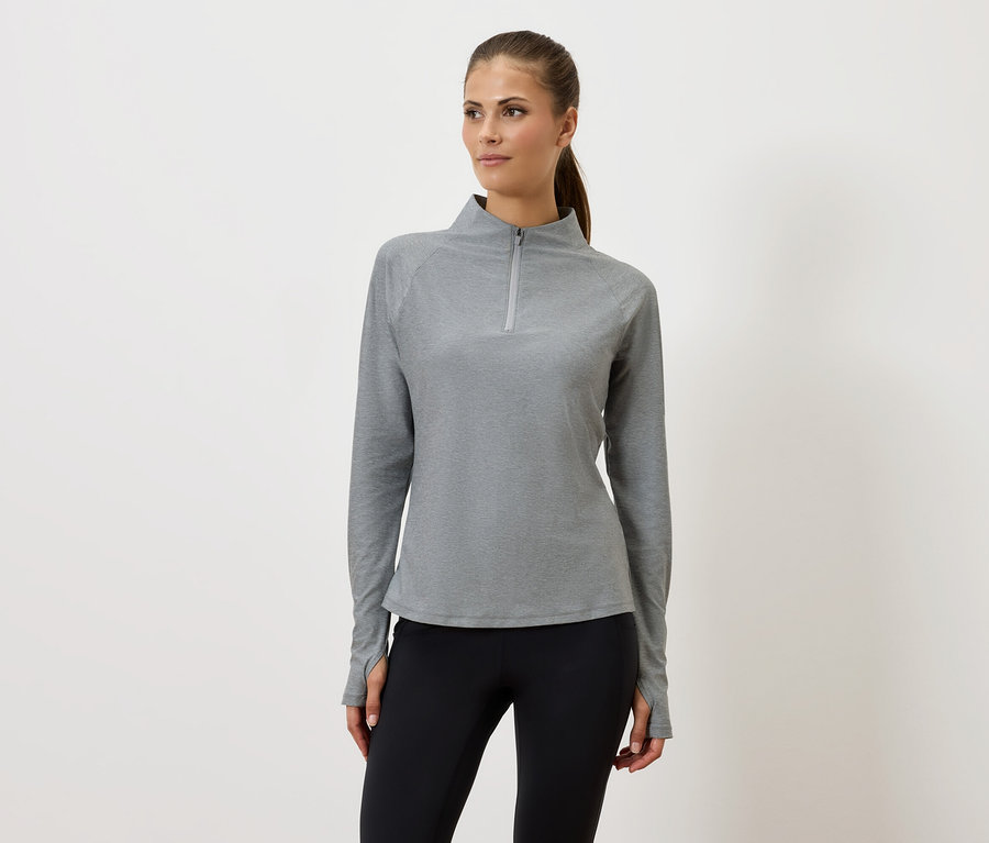 Žena v šedej mikine na zips a čiernych legínach stojí pred bielym pozadím.
