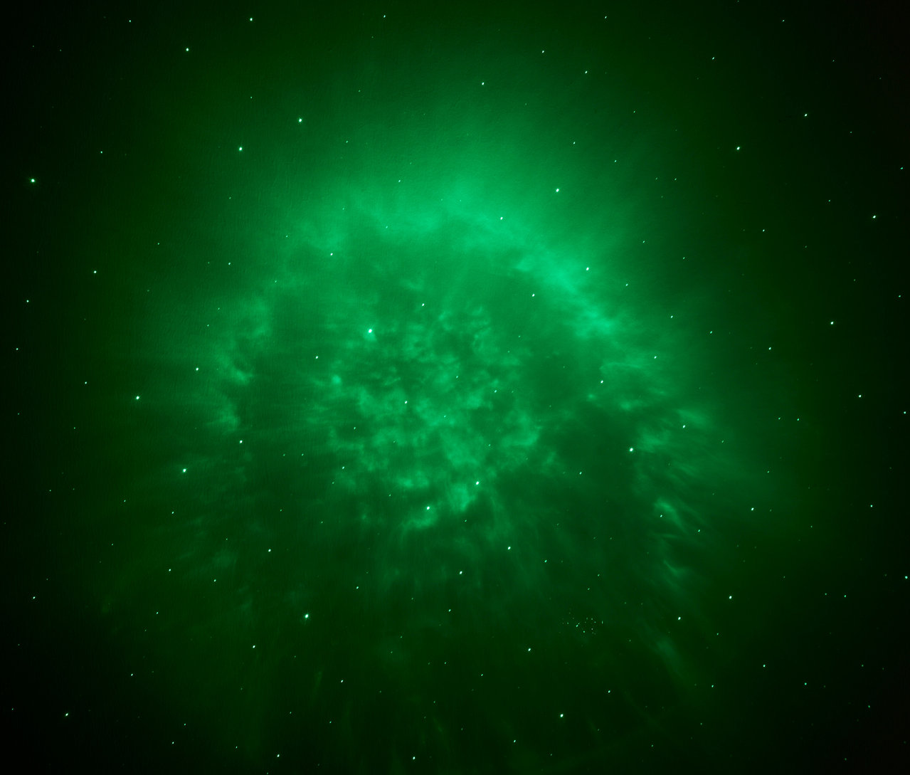 Zelená hmlovina so svetelnými bodmi na tmavom pozadí.