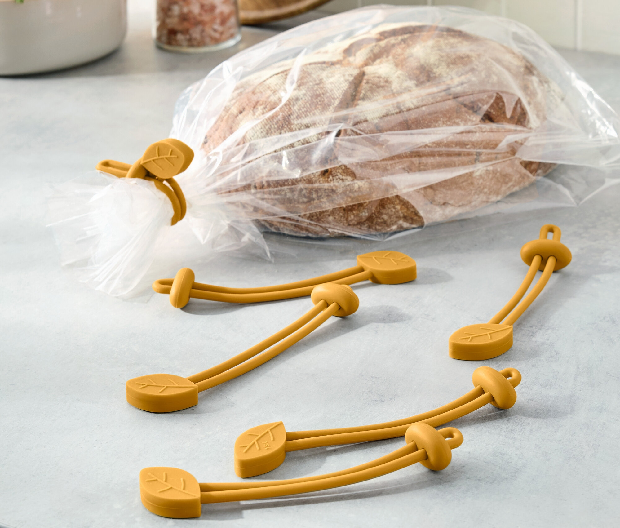 Chlieb v plastovom vrecku je uzavretý žltou gumičkou s motívom listu. Ďalšie tri gumičky ležia vedľa.