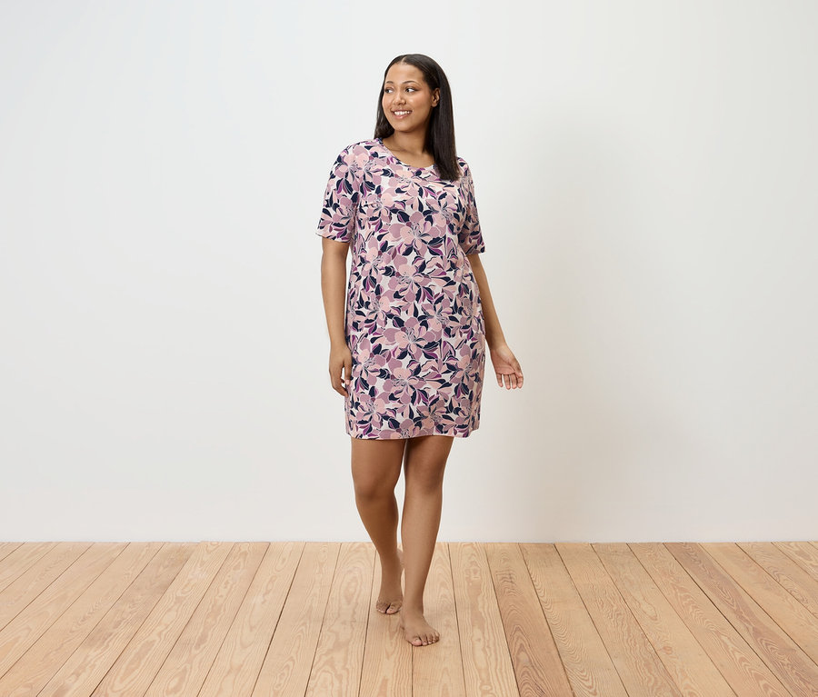 Žena kráča naboso po drevenej podlahe a má na sebe kvetinové šaty.