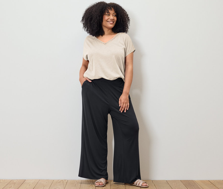 Žena pózuje v krémovobielom tričku zo zmesi modalu a čiernych nohaviciach v štýle palazzo.