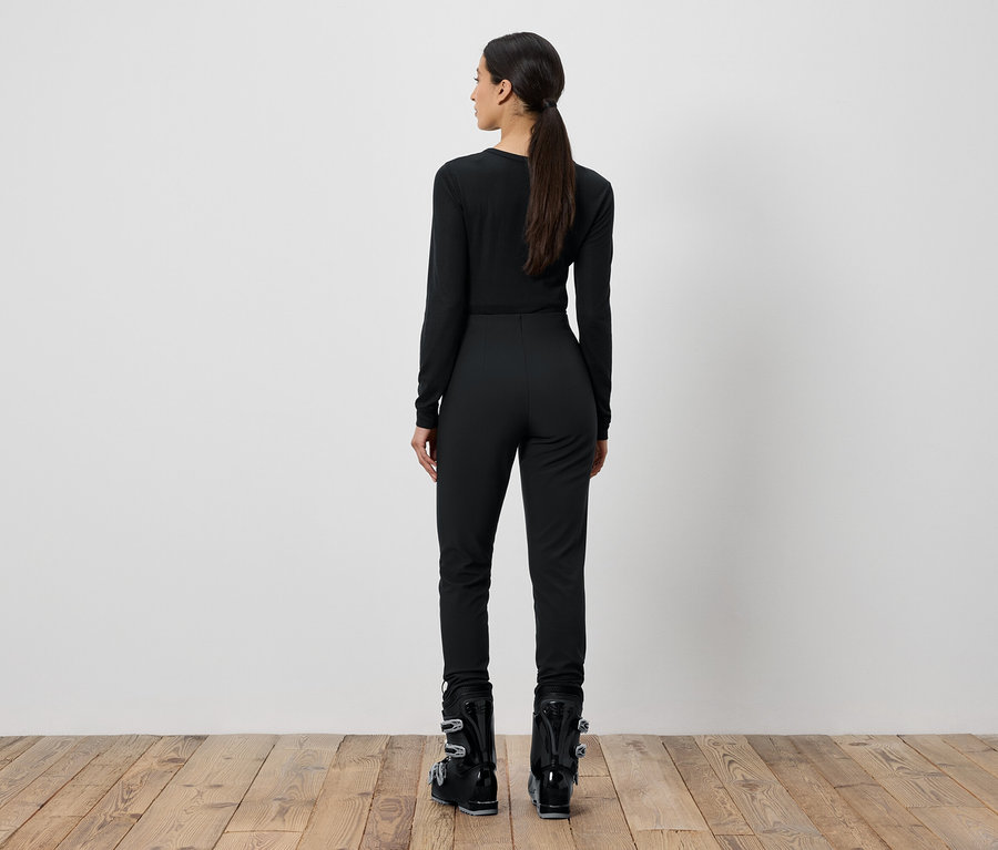 Žena v čiernom lyžiarskom oblečení stojí chrbtom.