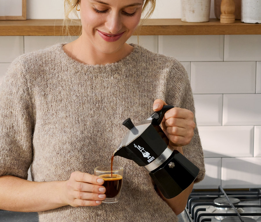Žena nalieva kávu z čierneho kávovaru Bialetti Moka Express, 190 ml, do šálky.