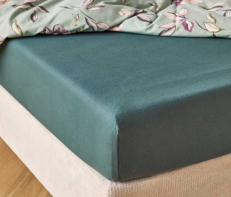 Detailný záber na tmavozelený matrac s mätovo zelenou plachtou s kvetinovým vzorom navrchu.