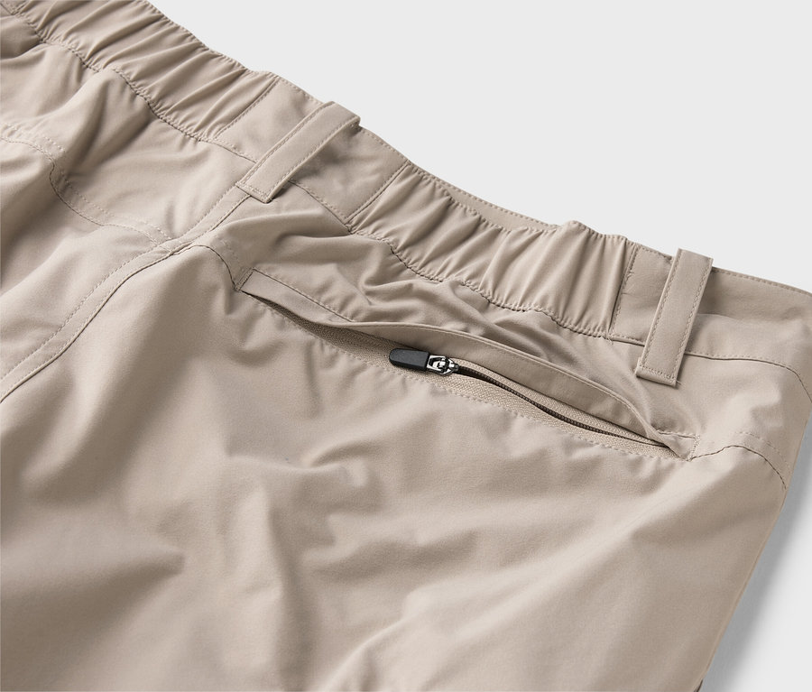 Detail béžových nohavíc s elastickým pásom a vreckom na zips.