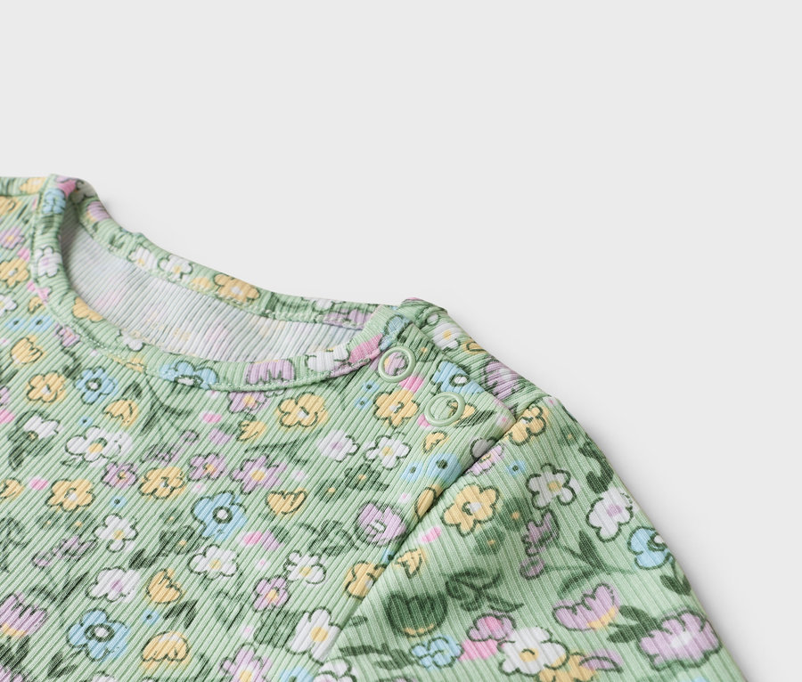 Detailný záber na svetlozelené detské body s kvetinovým vzorom a patentkami na ramene.