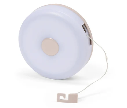 Detailný záber na okrúhlu, svetloružovú nočnú lampu so šnúrkou na bielom pozadí.
