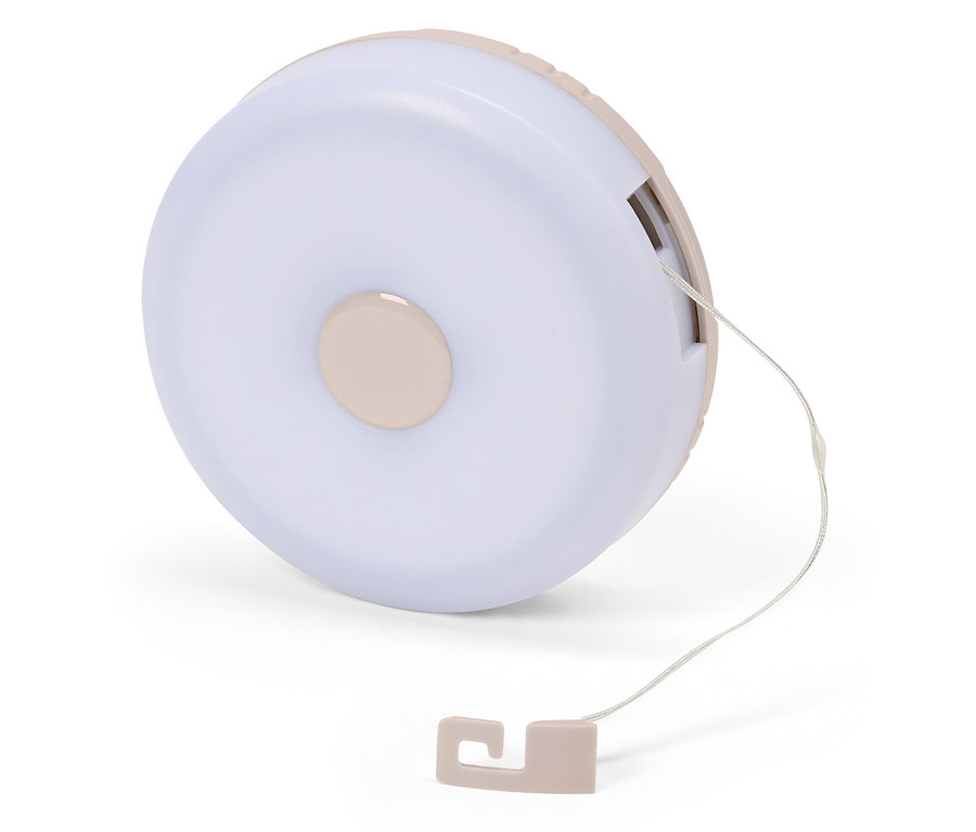 Detailný záber na okrúhlu, svetloružovú nočnú lampu so šnúrkou na bielom pozadí.