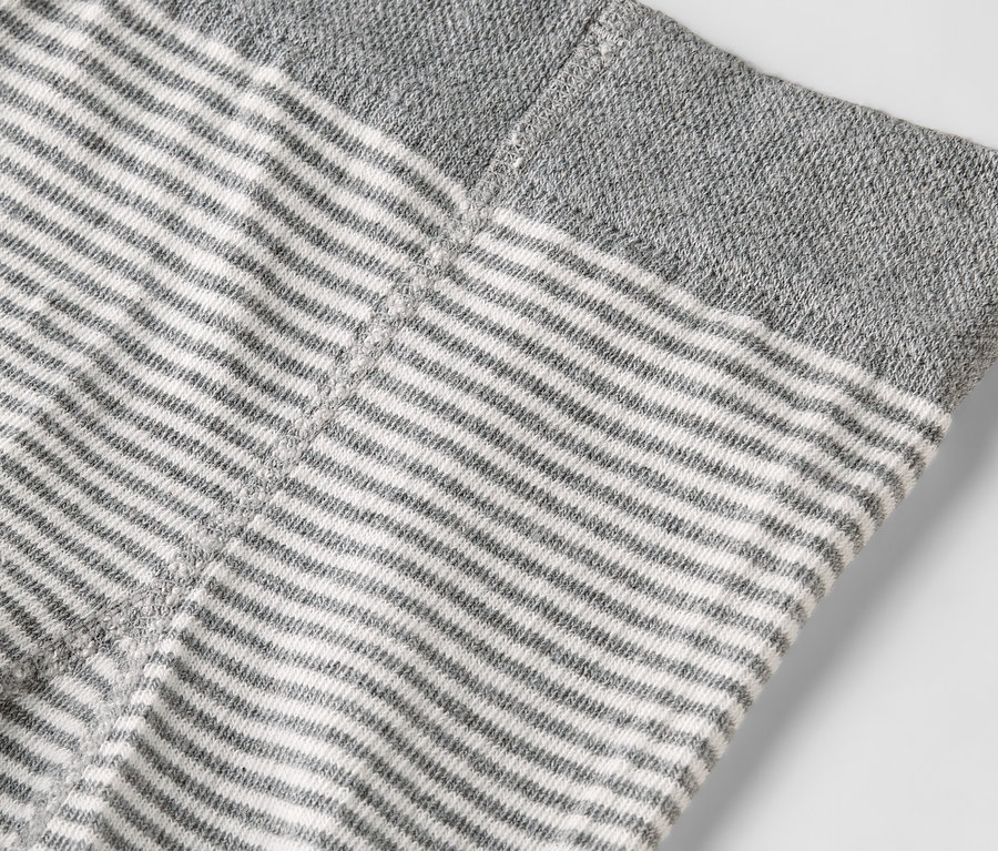 Detail odevu s vodorovnými sivými a bielymi pruhmi a sivým lemom.