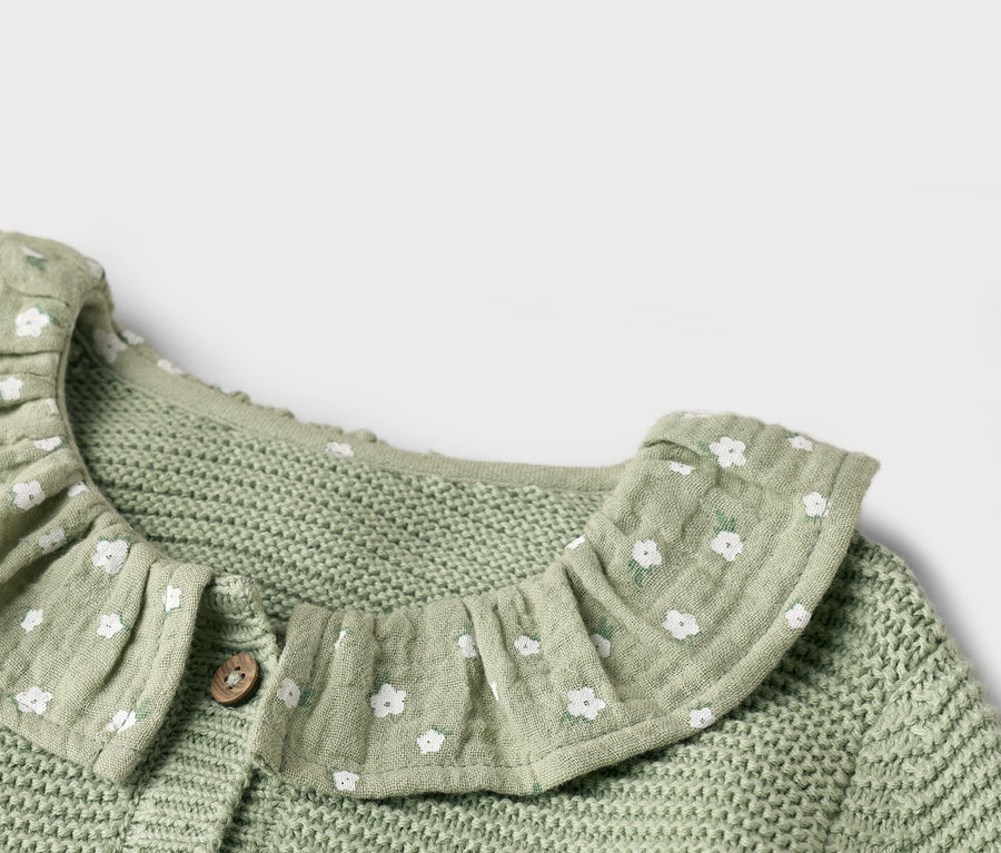 Detail svetlozeleného pleteného kardigánu s bielym kvetinovým vzorom a volánovým golierom.