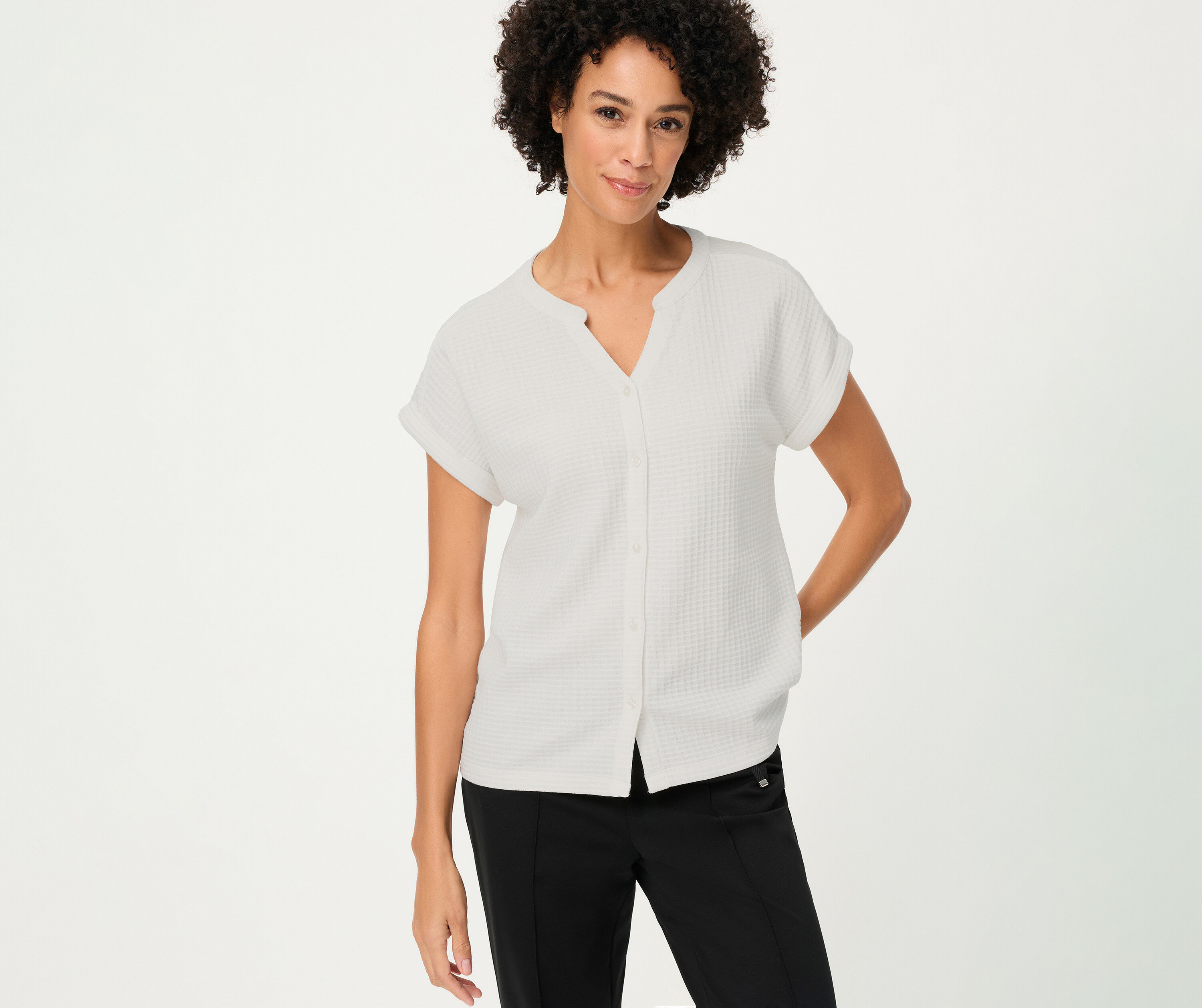 Žena s kučeravými vlasmi má na sebe štruktúrovanú košeľu Olsen s gombíkmi v bielej farbe a čierne nohavice.
