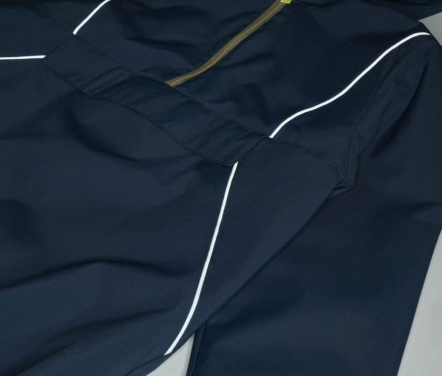 Detailný záber na tmavomodrú bundu s kapucňou a bielym pruhom, zapínanú na olivovozelený zips.