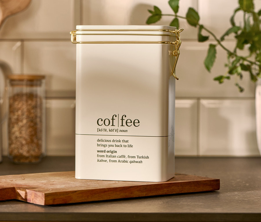 Biela dóza na kávu "coffee dictionary" stojí na drevenej doske.