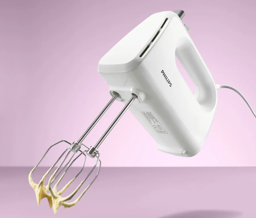 Biely ručný mixér Philips HR 3706 s nerezovými metličkami, na ktorých je žlté cesto.