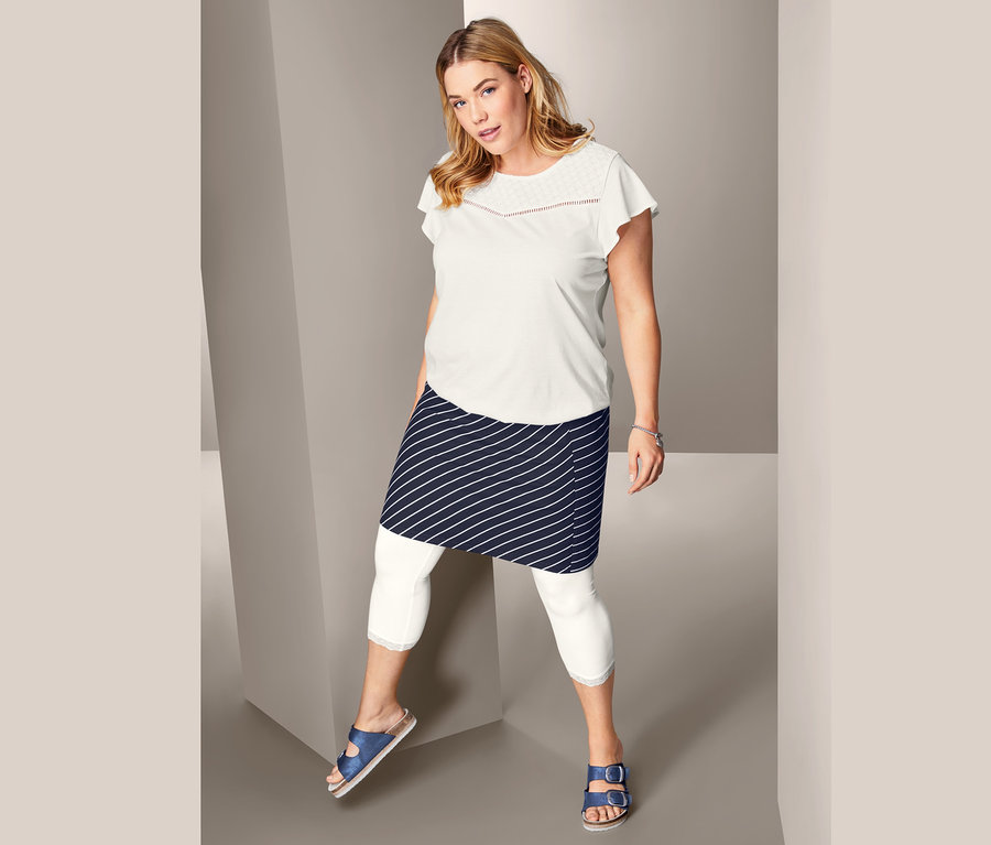 Žena pózuje v tričku s ažúrovou výšivkou, prúžkovanej džersejovej sukni a trojštvrťových legínsach s čipkovým lemom.