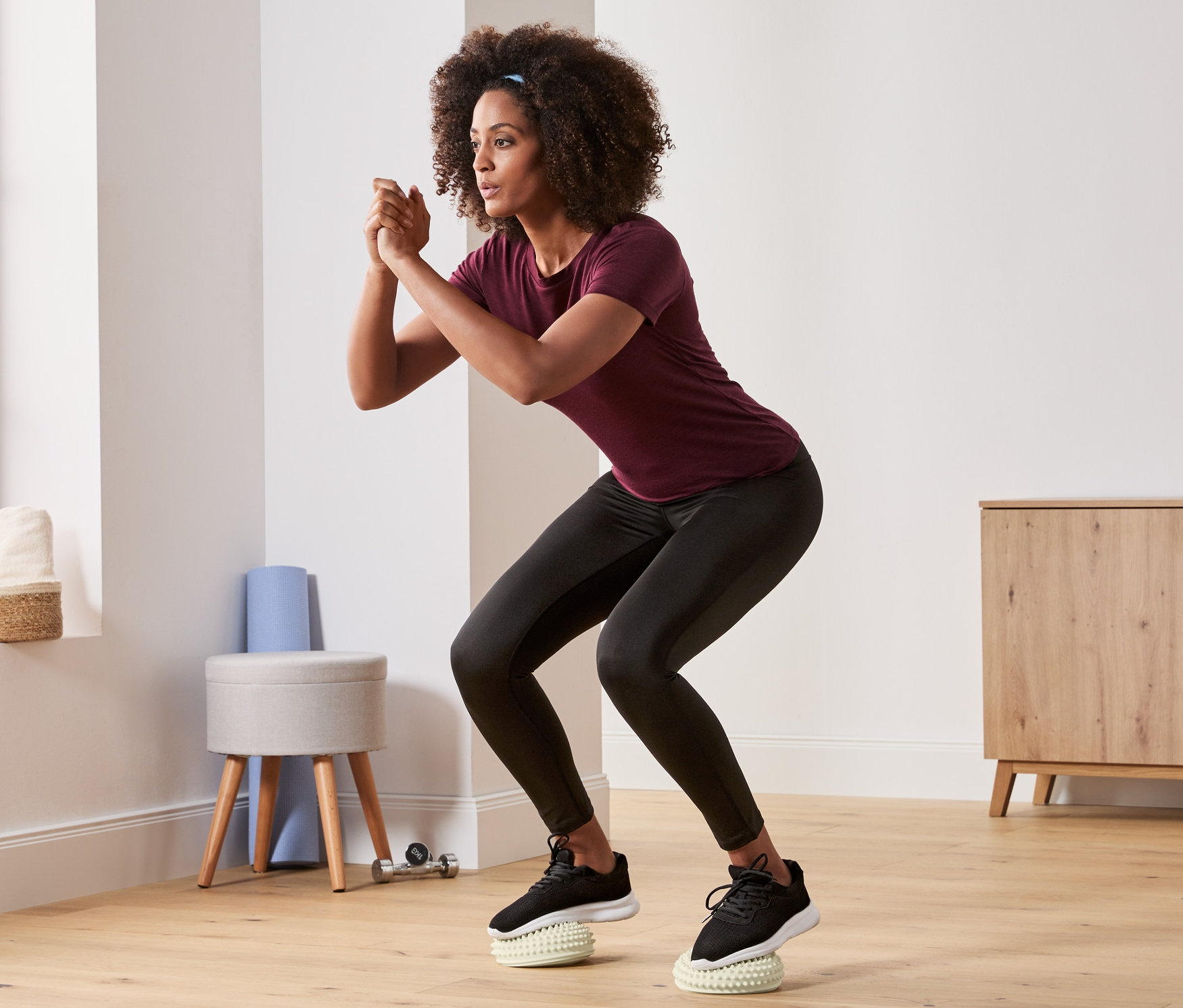 Žena v čiernych legínach a fialovom tričku robí drepy na balančných a masážnych podložkách, 2 ks.