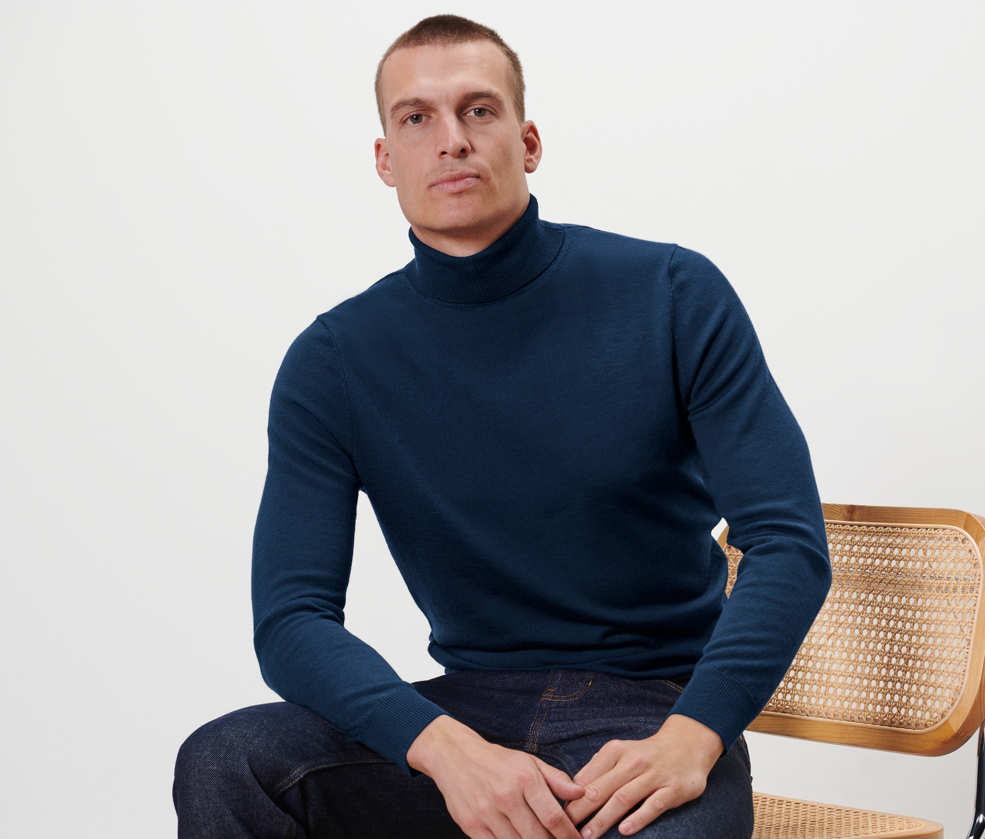 Muž sedí na stoličke a má na sebe pulóver z merino vlny, námornícka modrá.