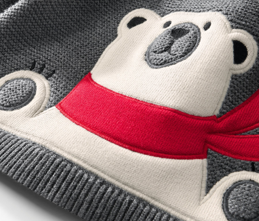 Detail detského pleteného pulóvra s aplikáciou ľadového medveďa s červeným šálom.