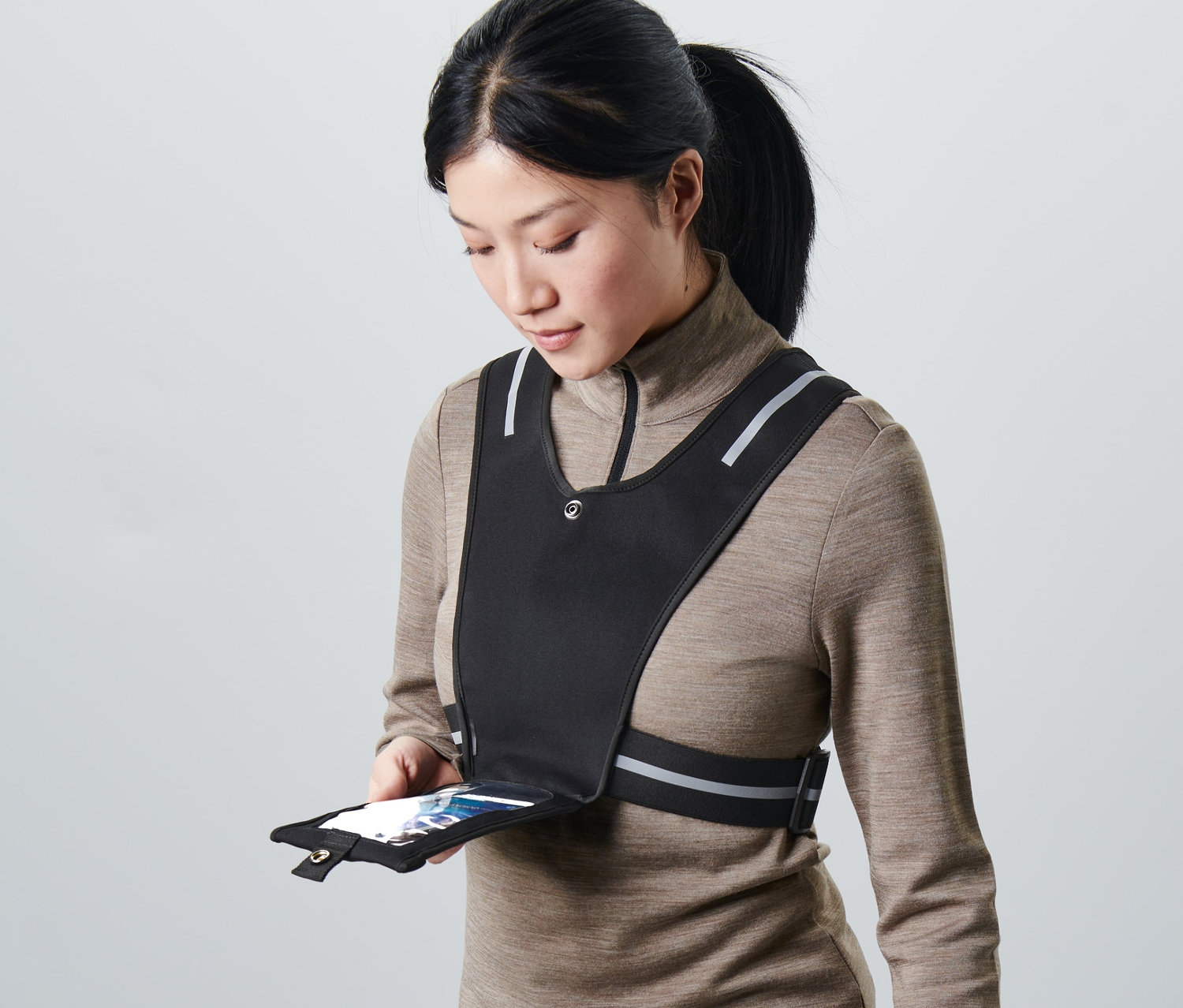 Žena drží smartfón vo vrecku čiernej bežeckej vesty.