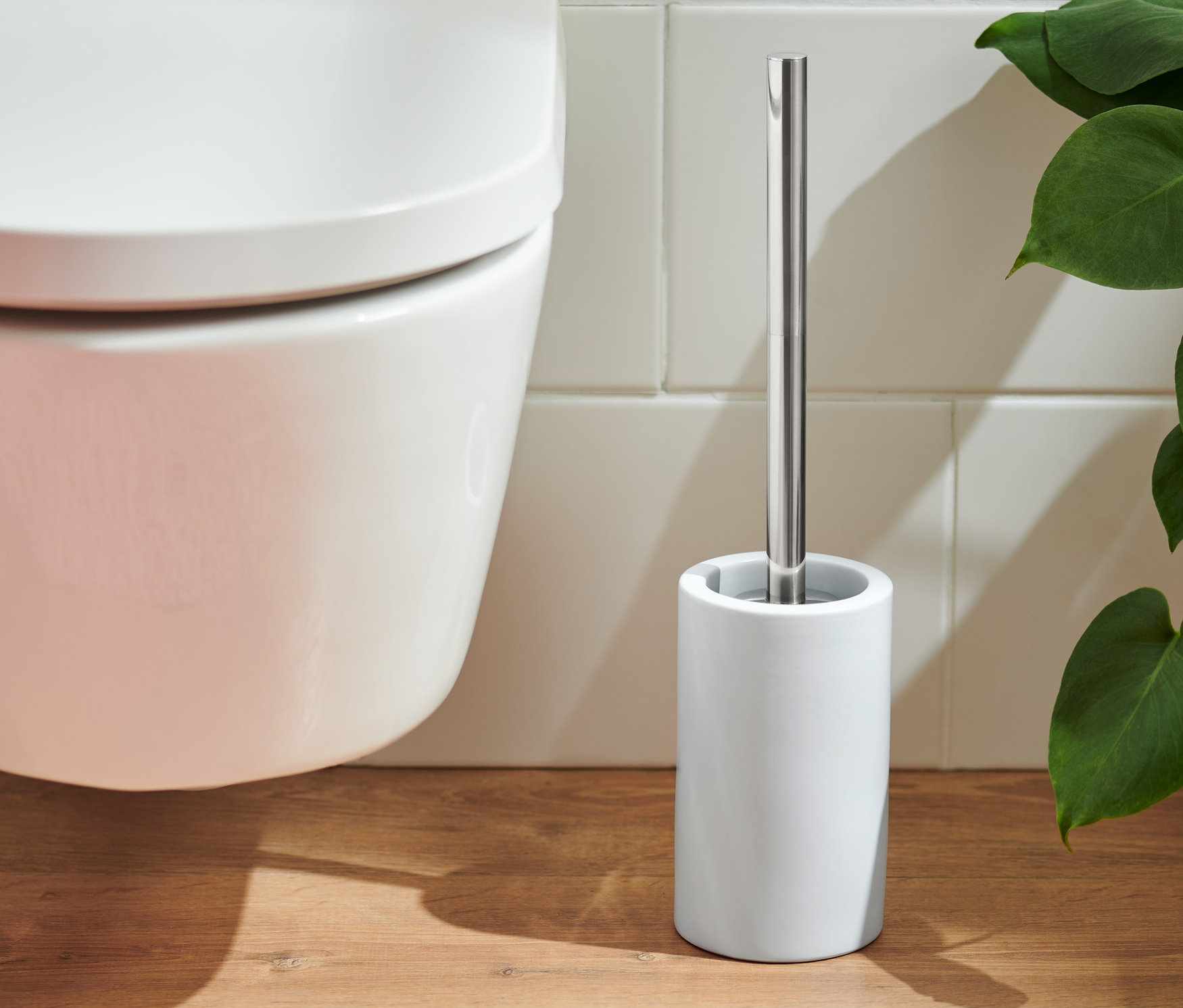 WC misa a biela WC kefa stojí na drevenej podlahe vedľa ružového koberca.