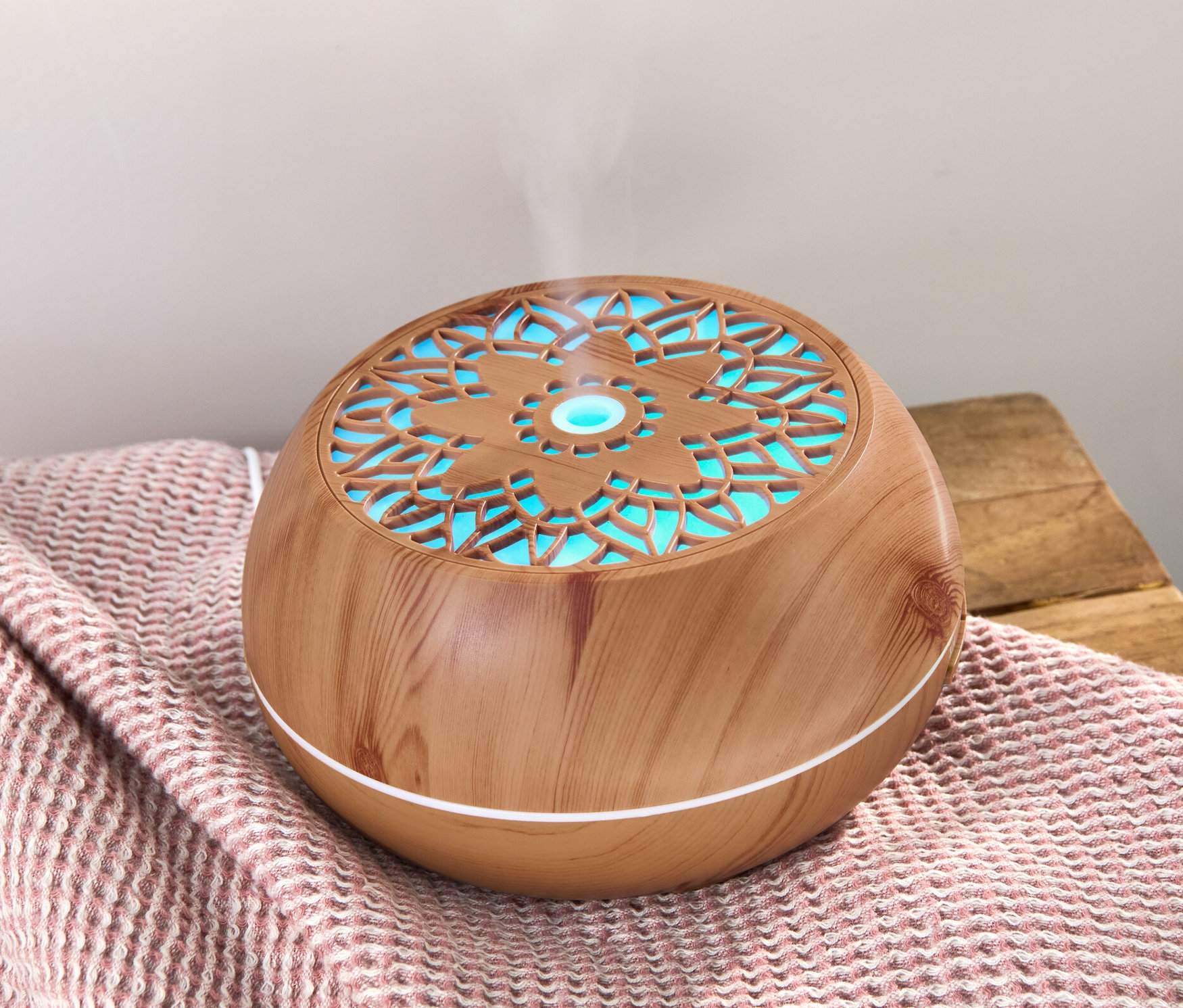 Aróma difuzér s Bluetooth® reproduktorom na ružovej deke, z ktorého stúpa para.