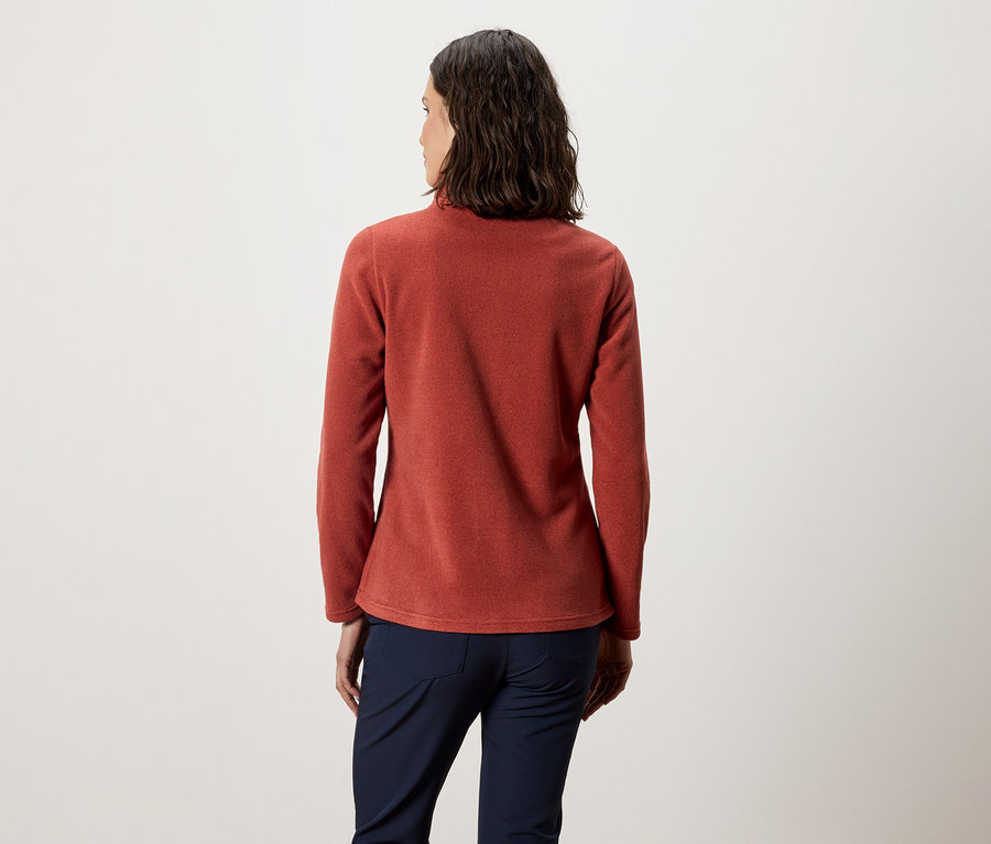 Žena chrbtom k fotoaparátu má na sebe oranžový flísový top a tmavomodré nohavice.