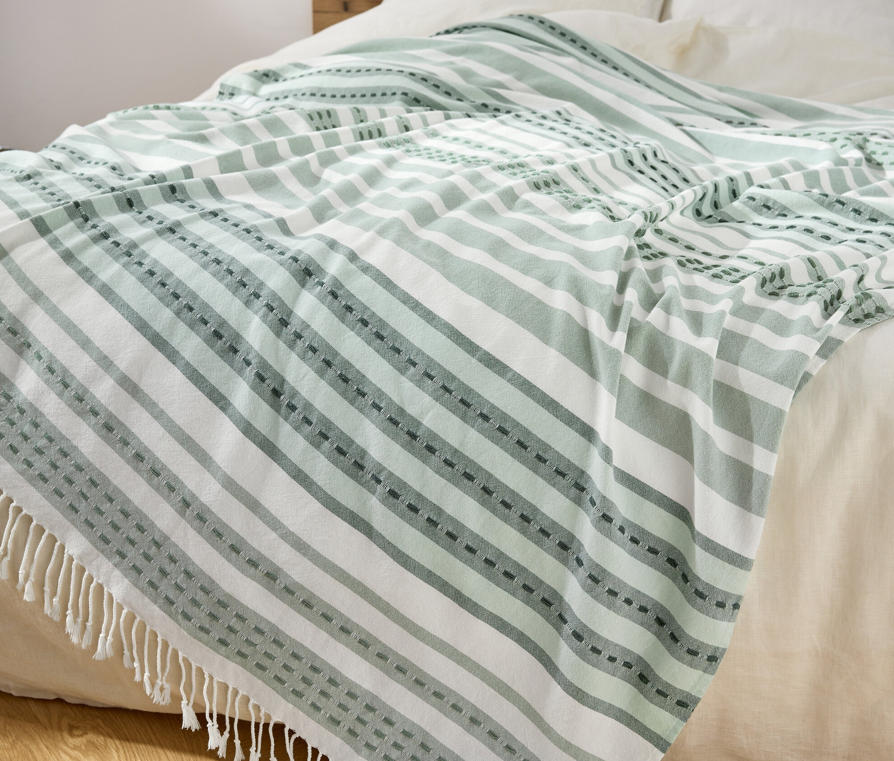 Na posteli leží pléd so zelenými a bielymi pruhmi a strapcami.