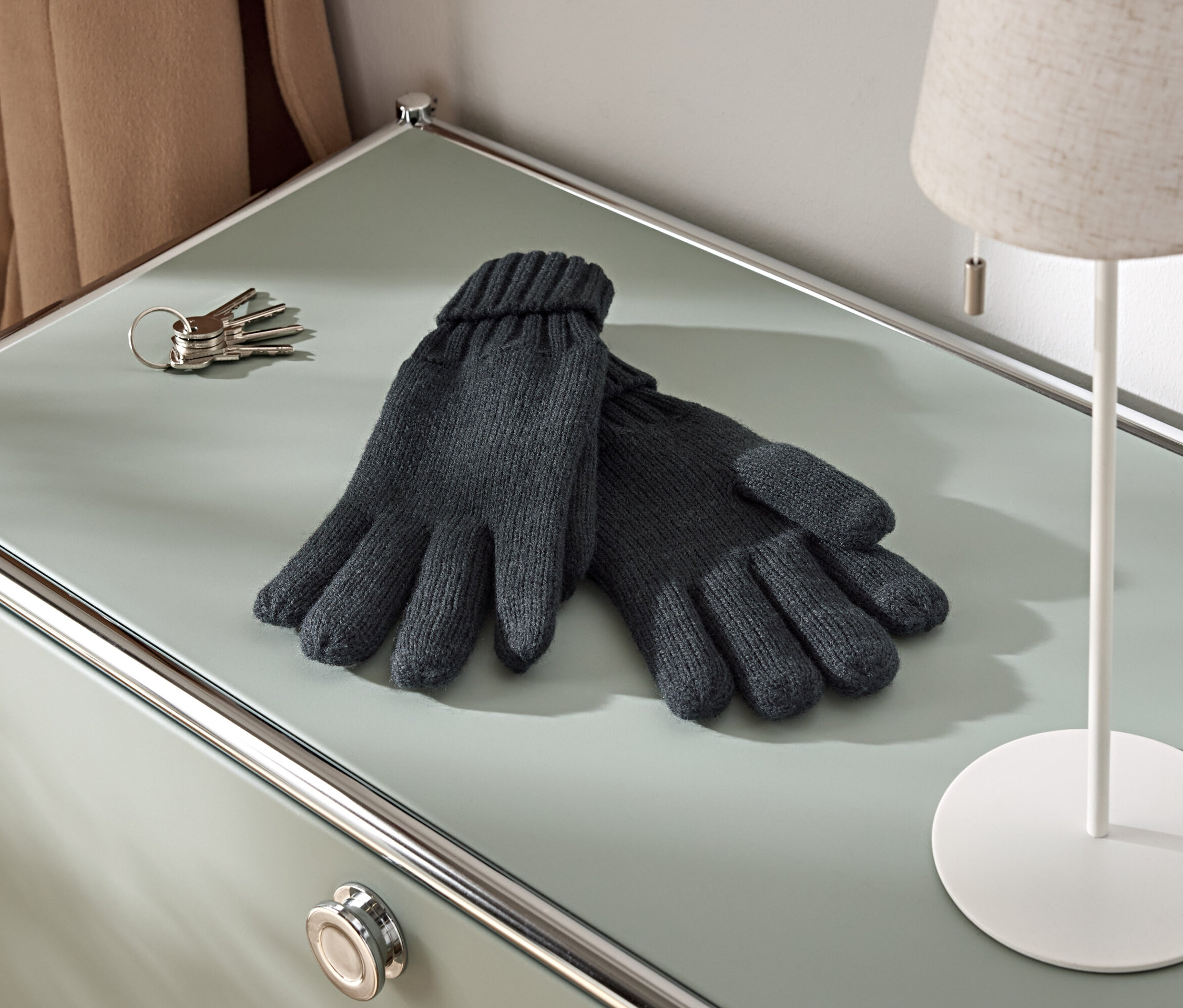 Na skrinke leží pár pletených rukavíc, zväzok kľúčov a lampa.