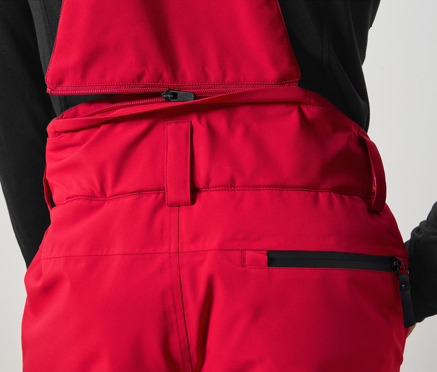 Detail červených nohavíc s trakmi a čiernym zipsom.
