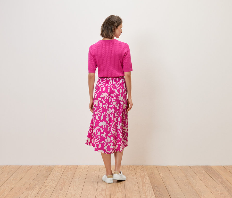 Žena chrbtom k fotoaparátu má na sebe ružový top a sukňu s kvetinovou potlačou.