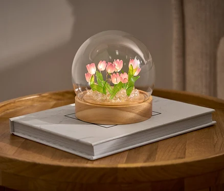 LED-DIY-Bastel-Set s tulipánmi v sklenenej kupole na knihe na okrúhlom stolíku.