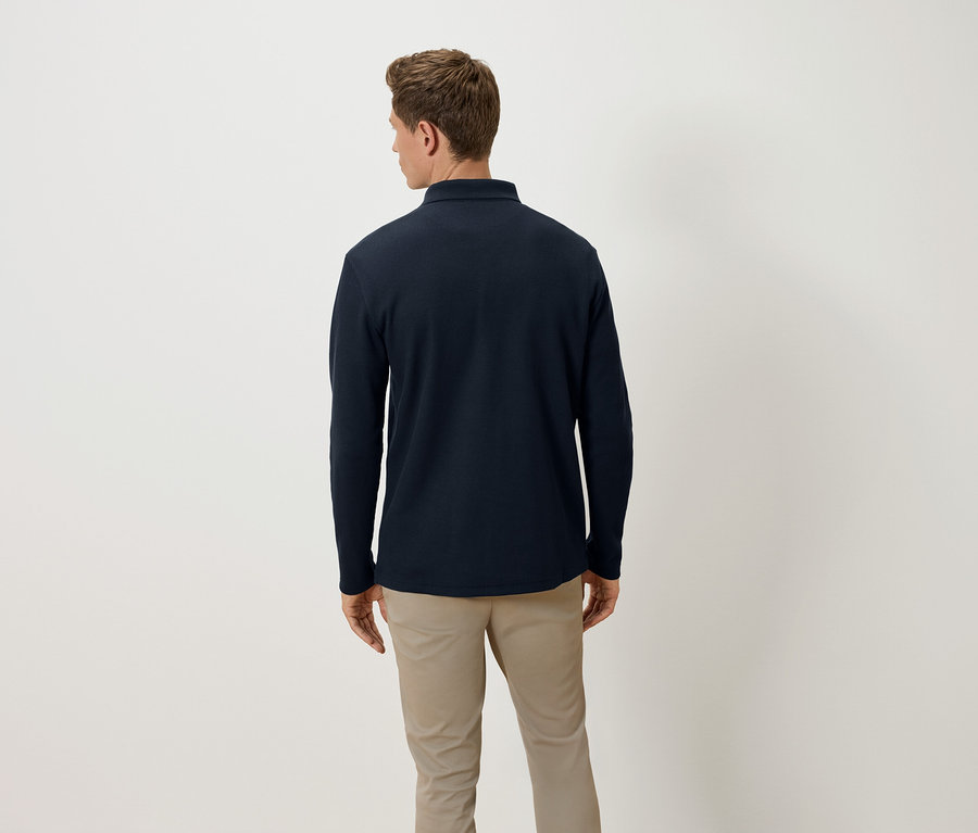 Muž chrbtom k fotoaparátu má na sebe tmavomodré polo tričko s dlhým rukávom a béžové nohavice.