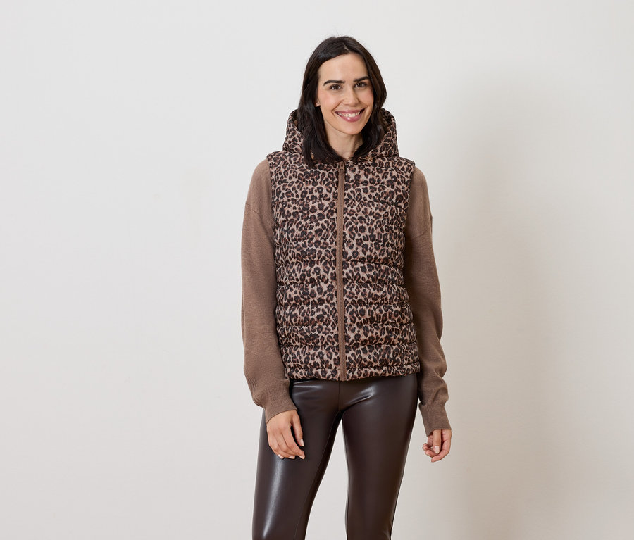 Žena pózuje v hnedej veste s kapucňou so zvieracím vzorom a hnedých kožených nohaviciach.