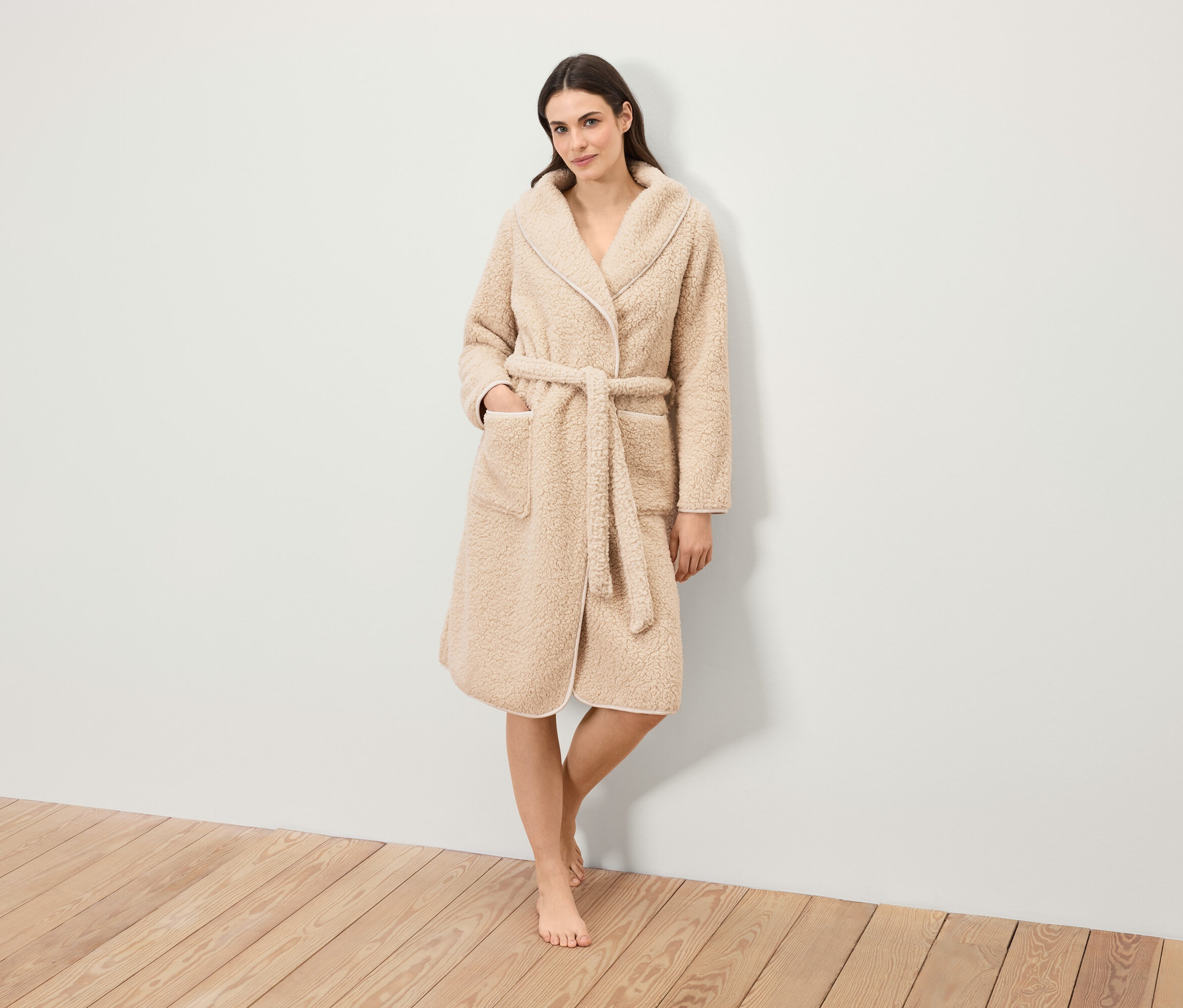 Žena stojí a má na sebe huňatý župan s opaskom.