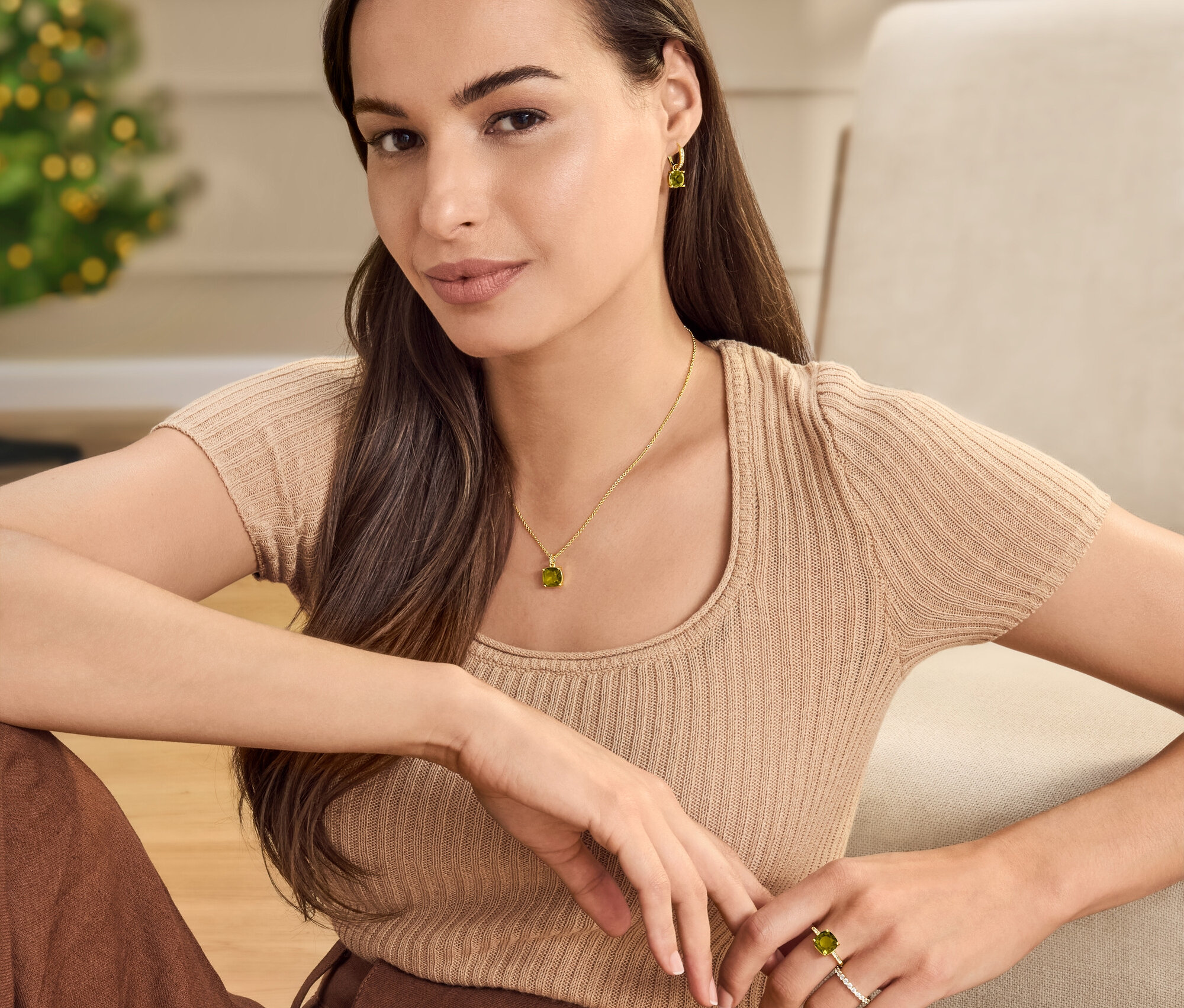 Žena sedí s retiazkou, kruhovými náušnicami a prsteňom so zeleno-hnedým skleneným krištáľovým kamienkom.