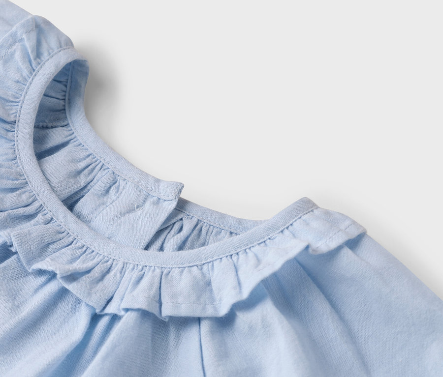 Detailný pohľad na svetlomodrý látkový top s volánovým golierom.