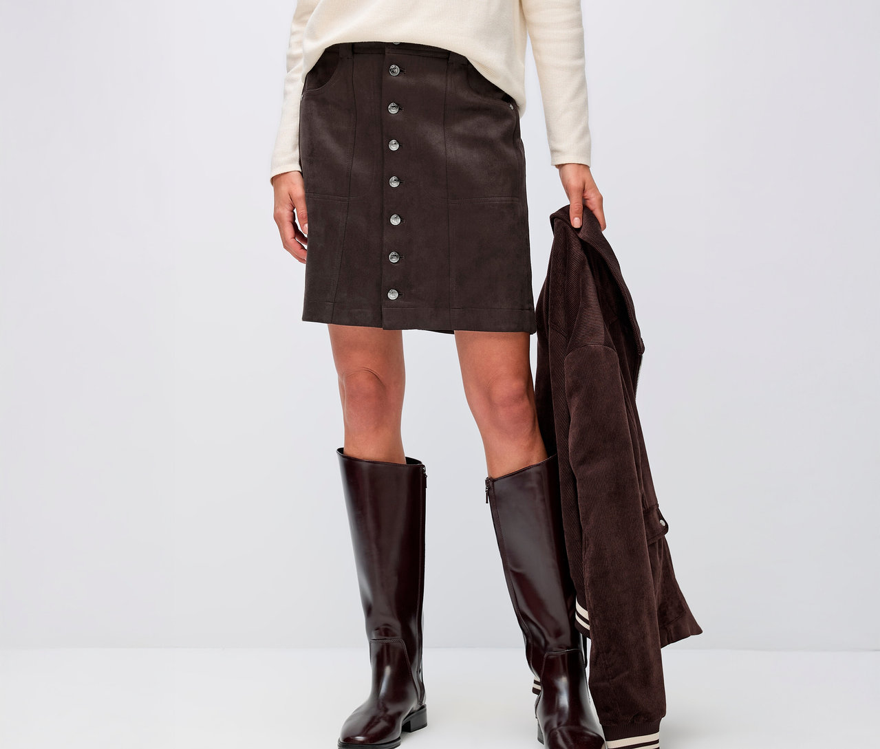 Žena má na sebe Street One velúrová sukňa, krémový top a hnedé čižmy.